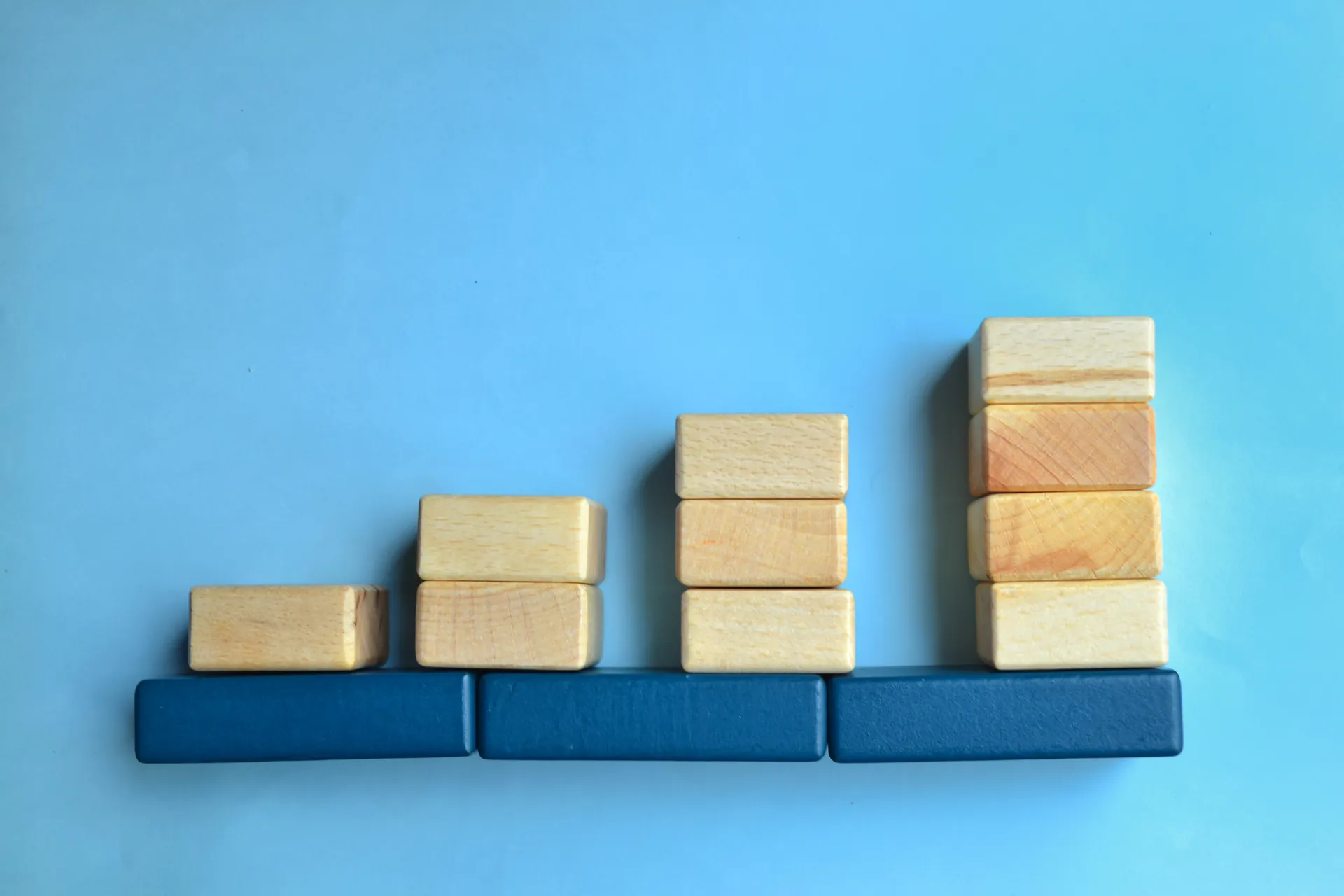 Blocos de madeira empilhados em escada crescente sobre fundo azul — construção incremental de MVP